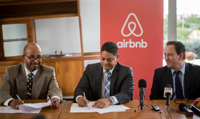O ministro do Desenvolvimento Econômico de Curaçao, Eugene Rhuggenaath, assina o acordo, observado pelo ministro das Finanças, Kenneth Gijsbertha e pelo representante da Airbnb para o Caribe e América Central, Shawn Sullivan
