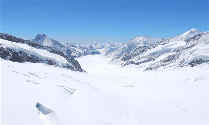 Vista das montanhas dos Alpes Suíços a partir da estação; sob sol forte, o branco da neve pode cegar momentaneamente os desavisados