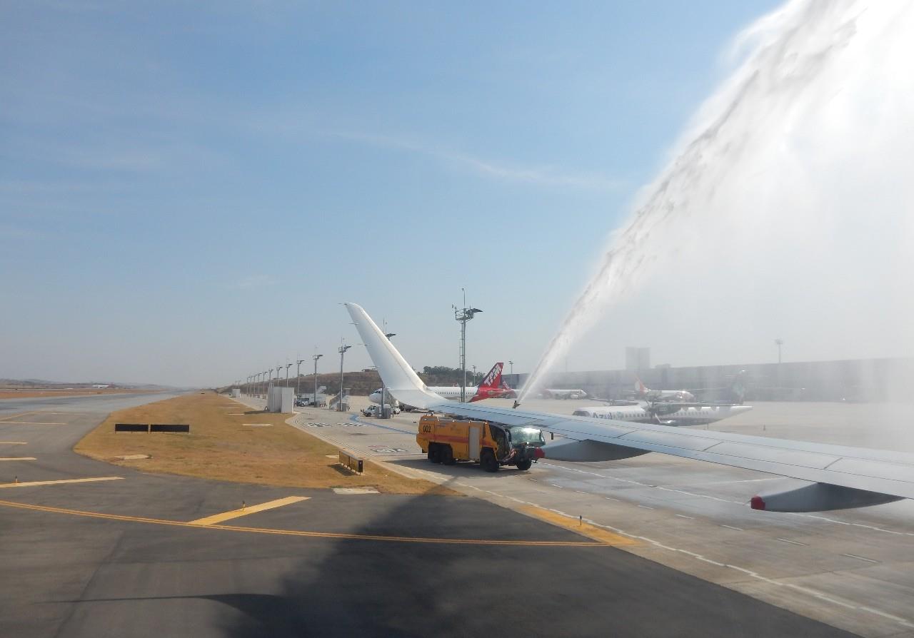 Caminhão de bombeiro lança jato de água sob aeronave na chegada em Belo Horizonte, em dia ensolarado