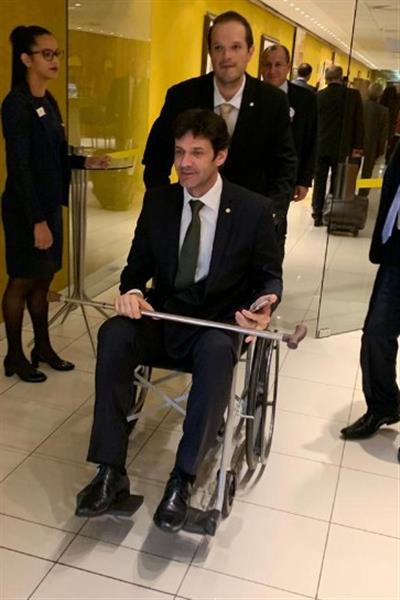 Com problemas no joelho, o ministro do Turismo está se locomovendo com a ajuda de uma cadeira de rodas