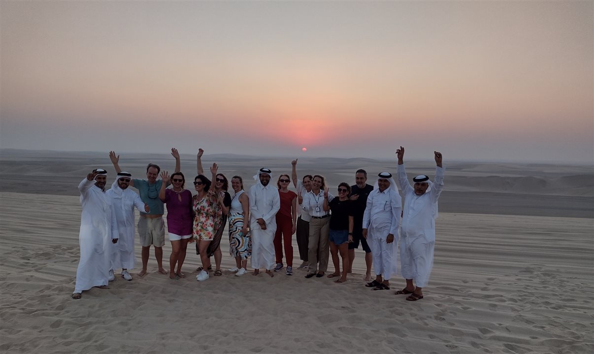 Os quatro motoristas, a guia de turismo Adriana e o grupo da Flot celebram o pôr-do-sol na duna do deserto