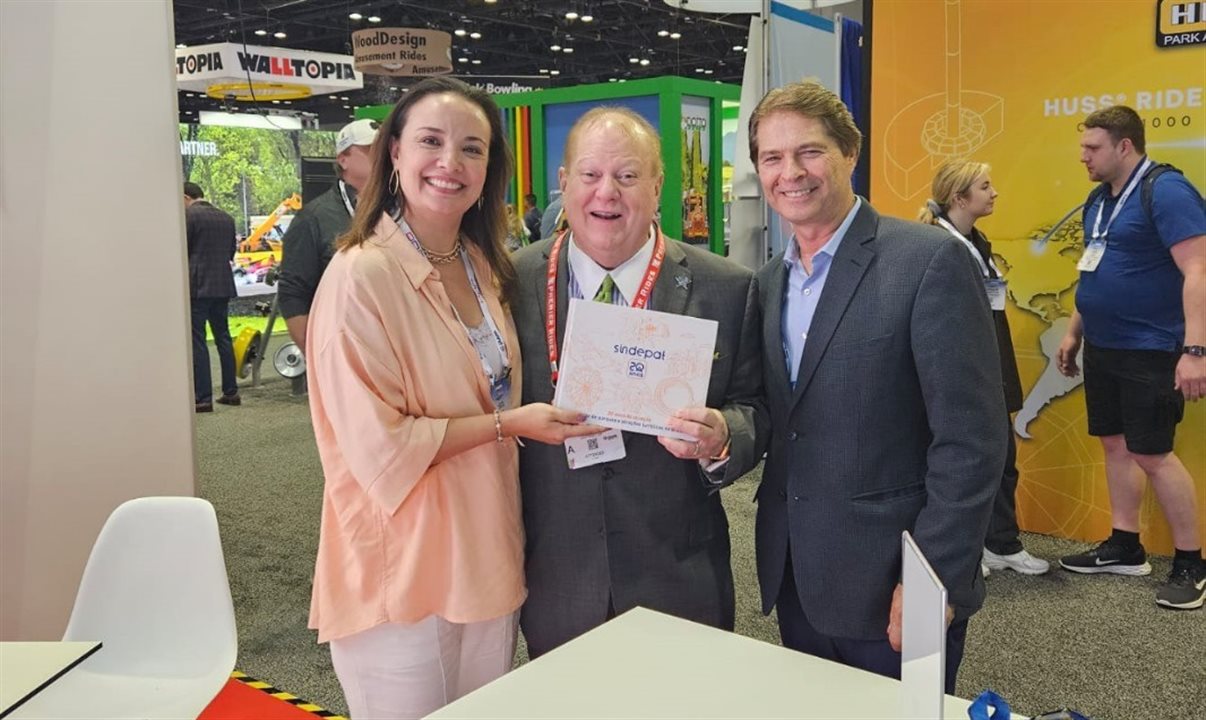 Carolina Negri entrega ao CEO da International Theme Park Services, Dennis Spiegel, livro que comemora os 20 anos do Sindepat, acompanhado pelo presidente de honra da associação, Alain Baldacci