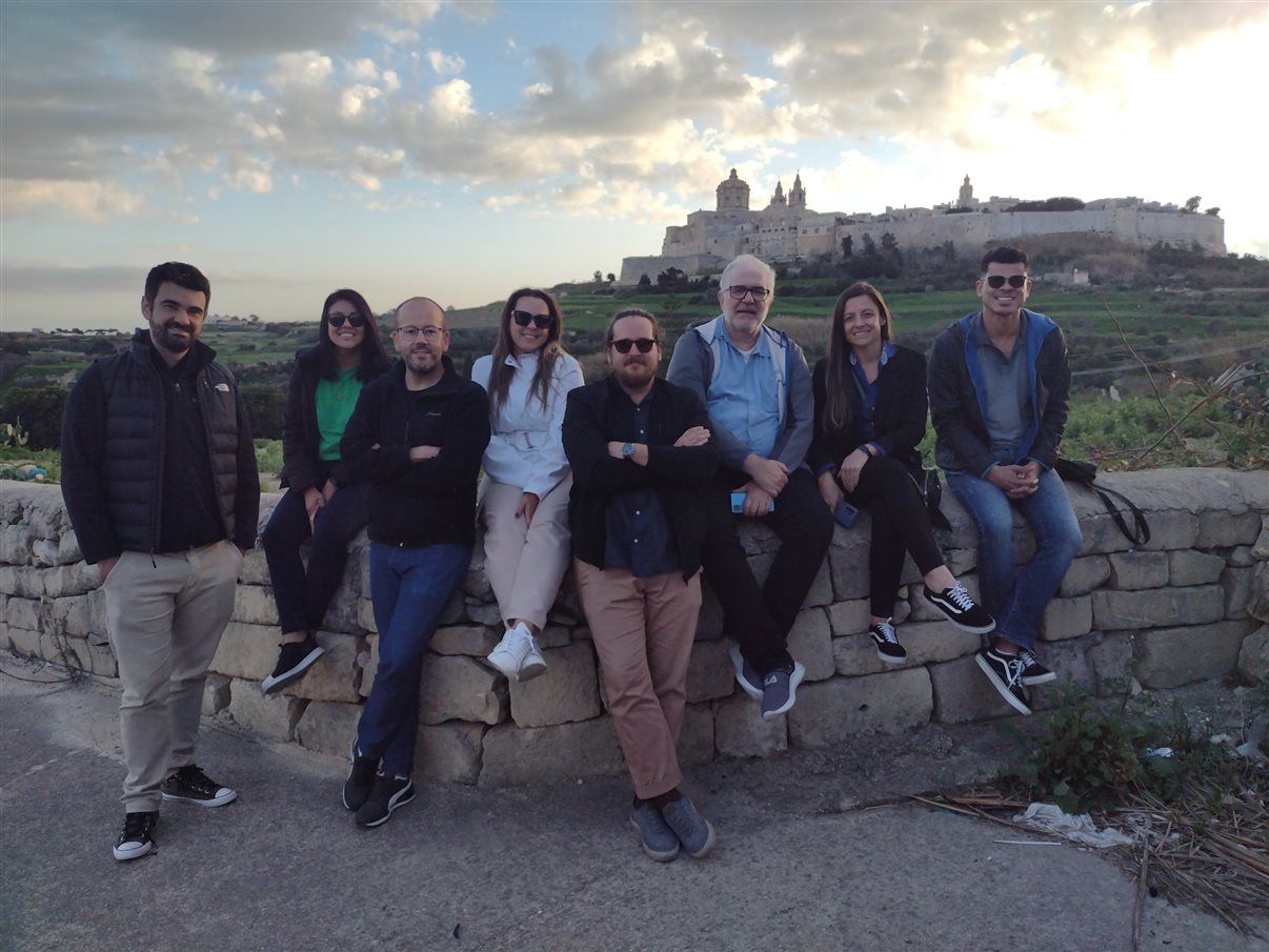 Grupo do famtour posa com complexo religioso murado, ao fundo, em Malta