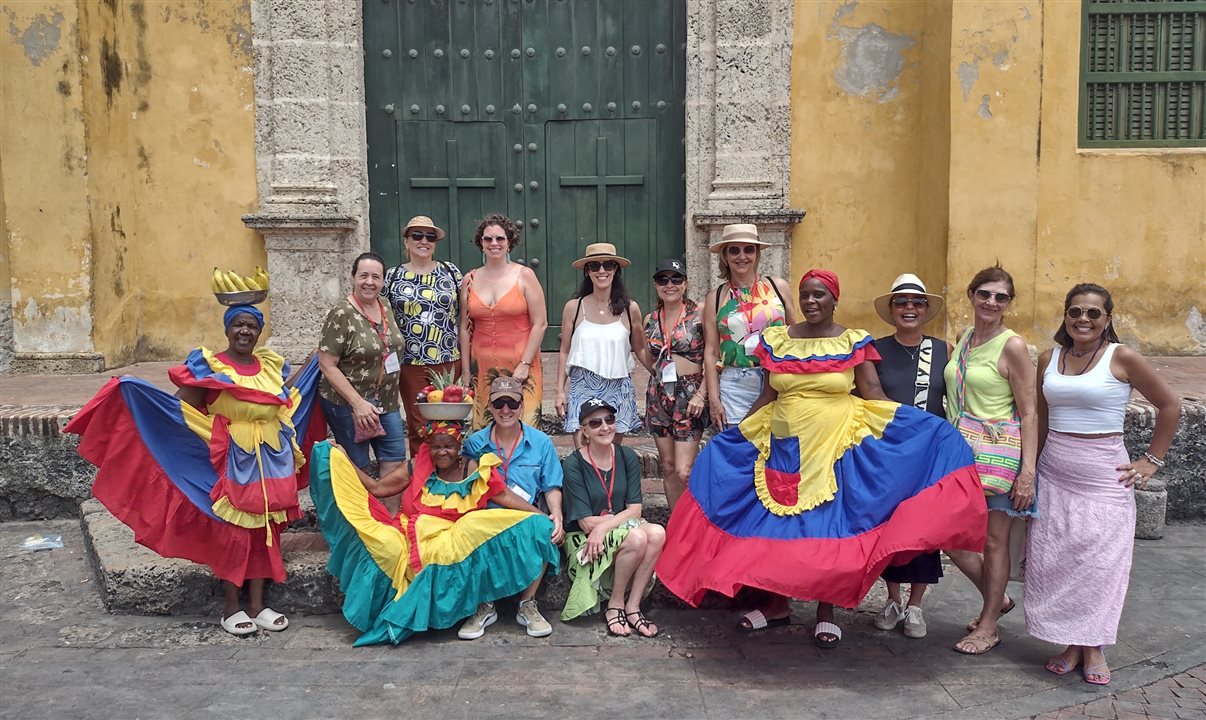 Grupo da Flot posa junto com três “palenqueras”, cujo trabalho é sair em fotos com turistas mediante o recebimento de um cachê, em frente à Igreja da Santíssima Trindade, em Getsemani, no Centro Histórico de Cartagena de Indias