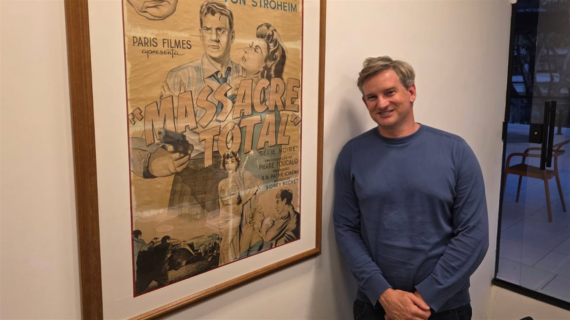 Sandi Adamiu, s&oacute;cio do Sandi Hotel, ao lado do primeiro cartaz de um filme distribu&iacute;do pela Paris Filmes no Brasil